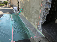 ライオンホームの塀塗装リフォーム。塗装の前に、塗料が付いてはいけない場所を守る養生の様子です。ビニールでその場所を保護しています。