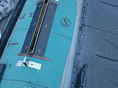 ライオンホームで屋根葺き替えリフォーム。大屋根に棟換気の金具を取り付けるところです。周りに緑色の防水シートが見えています。