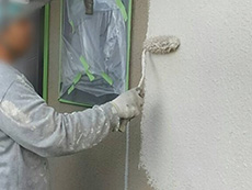 西京区の外壁塗装外構リフォーム。外壁に手塗ローラーで塗料を塗っています。2回目からは色の塗料を塗っていきます。