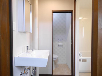 大山崎町の中古マンションリフォーム。リフォーム後の洗面室。洗面台ではなく、白い四角の洗面ボウルと壁に鏡を付けたシンプルなスタイルです。奥にトイレがあり、右手にお風呂場があります。