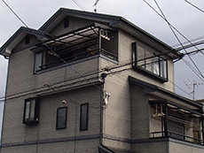 大山崎町の外壁塗装リフォーム。塗装前の外観です。濃いグレーの窯業系サイディングの建物です。