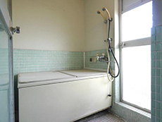 大山崎町の円団団地リノベーション。リフォーム前のお風呂場です。浴槽の周りは水色のタイル張りになっています。浴室の中にバルコニーに出るドアがついています。
